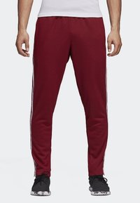 Maroon athletic pants with white side stripes, elastic waistband, and a smooth, soft fabric texture. Designed for comfort and movement.
