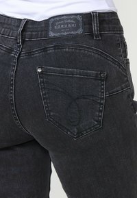 Juodi džinsai su formuota užpakaline kišene, dekoratyvine siuvinėta ir ženkleliu ant juosmens. Sklandus paviršius ir prigludusi išvaizda.