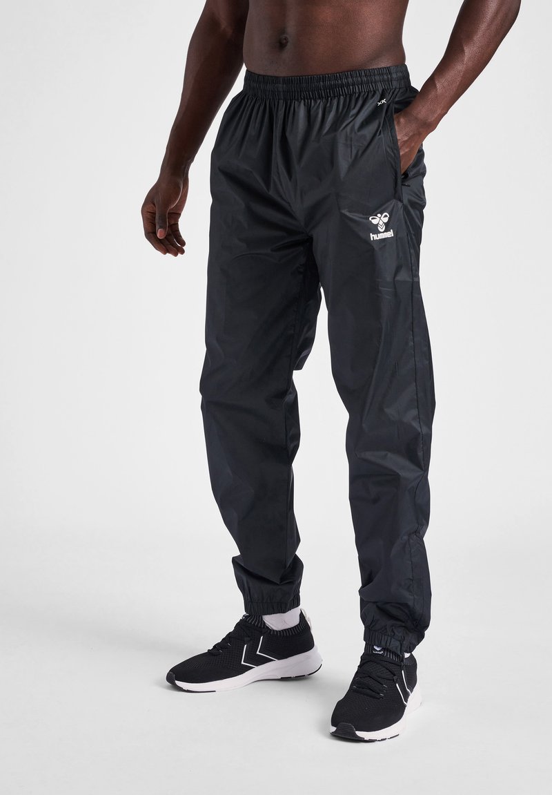 Svarta, lätta vindjackbyxor med elastisk midja och sidofickor. Har en logotyp på framsidan och manschettvidder.