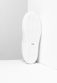 White sneaker with a rubber sole, textured zigzag pattern, and Italian flag accent. Smooth synthetic upper and padded collar.