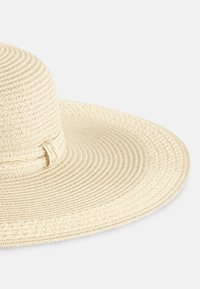 Szeroki kapelusz słomkowy w kolorze kremowym z teksturowanym, plecionym wzorem i ozdobnym, plecionym paskiem wokół korony.