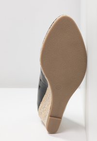 Semelle d'une chaussure compensée noire pour femme avec des côtés tissés et une semelle en gomme lisse couleur fauve, taille 37 marquée en dessous.