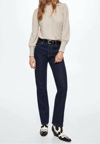 Beige tekstureret langærmet top, mørkeblå højtaljede jeans, sort bælte og unikke sorte og hvide hæle med udskåret design.