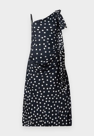 One-shoulder dress in navy fabric with white polka dots, featuring a side tie detail and ruched texture on the bodice.