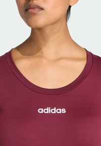 Bordeauxkleurig sportshirt met een ronde hals en een wit "adidas"-logo op de borst. Gladde textuur, aansluitend ontwerp.