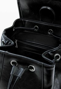 Mustast nahast õlakott koos paelaga kinnitamiseks, hõbedaste silmuste, sisemise tõmblukuga tasku ja siledapinna tekstuuriga. Avatud ülaosa paljastab avara sisu.