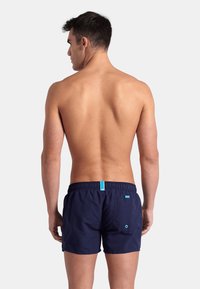 Pantaloni da nuoto blu navy con vita elasticizzata e dettagli turchesi; presenta una tasca posteriore con un bottone a contrasto.