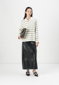 Striped long-sleeve shirt in soft fabric with white collar, paired with a black leather midi skirt and heeled black shoes. Clutch in hand.