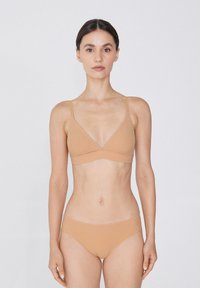 Beige nahtloser Bralette mit V-Ausschnitt und dünnen, verstellbaren Trägern, kombiniert mit passenden Bikini-Höschen mit einem tiefen Schnitt.