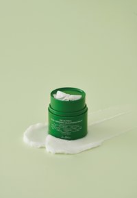Zielony cylindryczny słoik z białą wewnętrzną pokrywką, oznaczony napisem "Dr. Althea Pure Grinding Cleansing Balm", na jasnozielonym tle, z białą teksturą balsamu.
