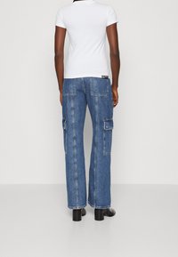 Breda cargojeans i medelblå denim, med sidofickor och rå nederkant, i kombination med en åtsittande vit t-shirt. Svarta klackstövlar.