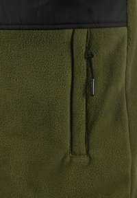 Olive green fleece fabric with a textured surface. Features a black horizontal panel at the top and a zippered pocket on the front.