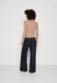 Ribbed long-sleeve top in beige, paired with dark blue wide-leg jeans featuring yellow stitching and back pockets.