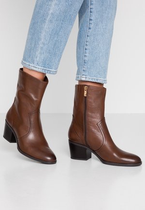 Braune Leder-Stiefeletten mit blockförmigem Absatz, seitlichem Reißverschluss, glatter Oberfläche und Nähten, kombiniert mit verkürzten hellblauen Jeans.