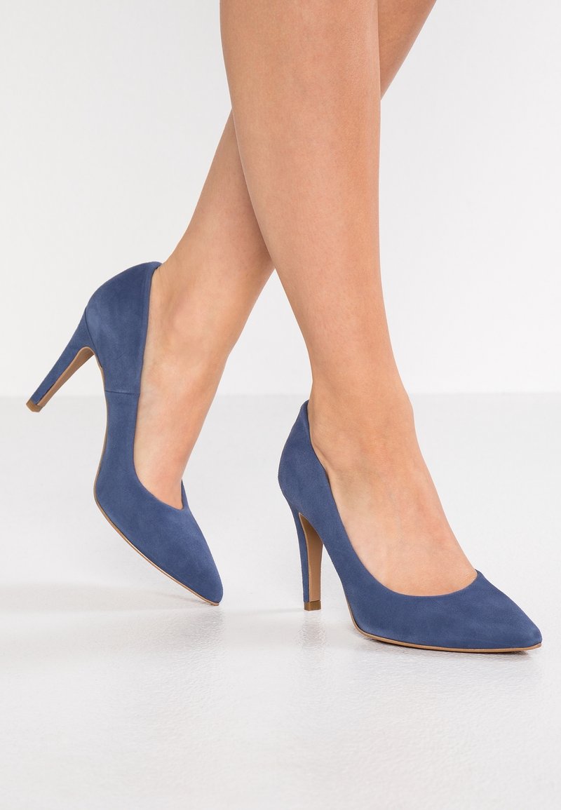 Escarpins en daim bleu avec bout pointu, talon stiletto mince, et texture lisse. Le design comporte un côté ouvert pour une apparence élégante.