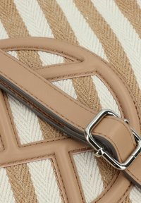 Beige leren band en hardware op een gestippelde tas met diagonale witte en tan strepen, met een opvallend geometrisch ontwerp.