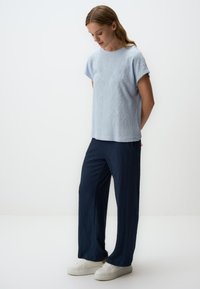 Lichtblauw gestructureerd T-shirt met korte mouwen, gecombineerd met donkerblauwe gestructureerde wijde broek en witte sneakers. Eenvoudige, strakke lijnen en een ontspannen pasvorm.