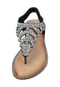 Sandal nera con design a foglia gioiello, dotata di una sottile striscia e di un inserto metallico per le dita, poggiata su una suola beige chiaro con bordi texturizzati.