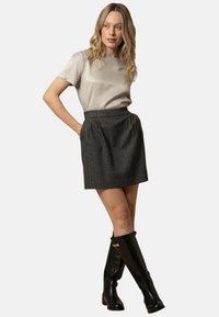 Gonna grigia a righe con pieghe, abbinata a una blusa beige chiara. Il modello indossa stivali neri in pelle al ginocchio. Design semplice e pulito.