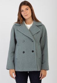 Cappotto doppiopetto in morbido tessuto grigio texturizzato. Presenta grandi bottoni neri, colletto a rovescio e tasche laterali. Vestibilità rilassata con spalle scese.