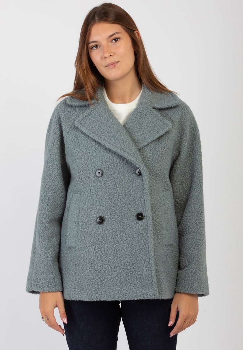 Cappotto doppiopetto in morbido tessuto grigio texturizzato. Presenta grandi bottoni neri, colletto a rovescio e tasche laterali. Vestibilità rilassata con spalle scese.