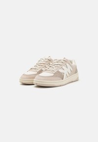 Sneaker beige realizzate in suede e mesh, dotate di un logo bianco, punta rotonda, chiusura con lacci e una parte superiore testurizzata. Suola in gomma.