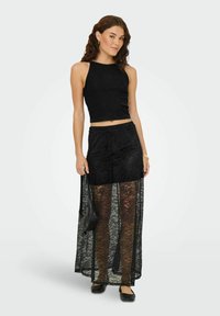 Černý žebrovaný crop top ve spojení s průhlednou černou krajkovou maxi sukni. Oblečení má přiléhavou siluetu a texturovaný krajkový vzor.
