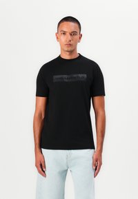 Svart t-skjorte med kort erm og matte svart rektangulære logo med "KARLLAGERFELD" over brystet. Glatt tekstur og klassisk passform.
