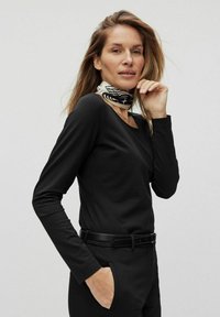 Svart långärmad topp med rund halsringning, matchad med svarta byxor och en mönstrad silkesjaal runt halsen. Slät textur, figursydd design.