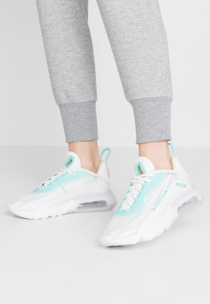 Baskets blanches et aqua avec une tige en maille transparente, amorti à air visible et lacets. Les accents incluent un branding bleu clair et une languette.