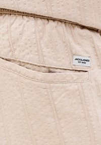 Bež teksturirani materijal s uzorkom okomitih pruga, malim džepom i bijelom ušivenom etiketom na kojoj piše "JACK & JONES EST. 1990."