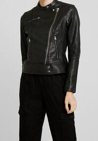 Svart läderbikerjacka med en asymmetrisk dragkedja, ståkrage och flera blixtlåsfickor. Tight passform med slät textur.