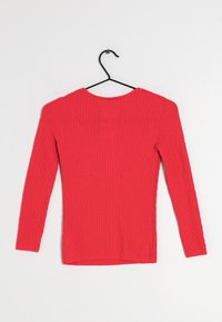 Röd ribbad långärmad topp med rund halsringning och en strukturerad mönster. Tillverkad av stickat material, hänger den på en svart krok.