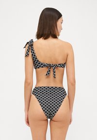 Bikini komplet v črno-beli vzorčasti kombinaciji z enostranskim vrhom, ki ima nagajiv pripomoček za vezanje, in visokim pasom, izdelan iz gladkega materiala.