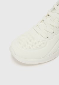 Baskets blanches de sport dotées d'un dessus texturé avec des perforations, des lacets plats et une semelle en caoutchouc lisse. Design minimaliste avec des accents courbés.
