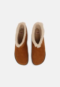 Brune ankelstøvler i suede med faux fur-fôr, rund tå og svart gummisåle. Har et enkelt, sømløst design uten synlig maskinvare.