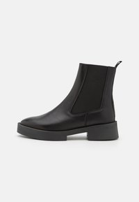 Botas de tobillo de cuero negro con paneles laterales elásticos, punta redondeada y suela de goma gruesa. Acabado suave con una lengüeta en la parte trasera.