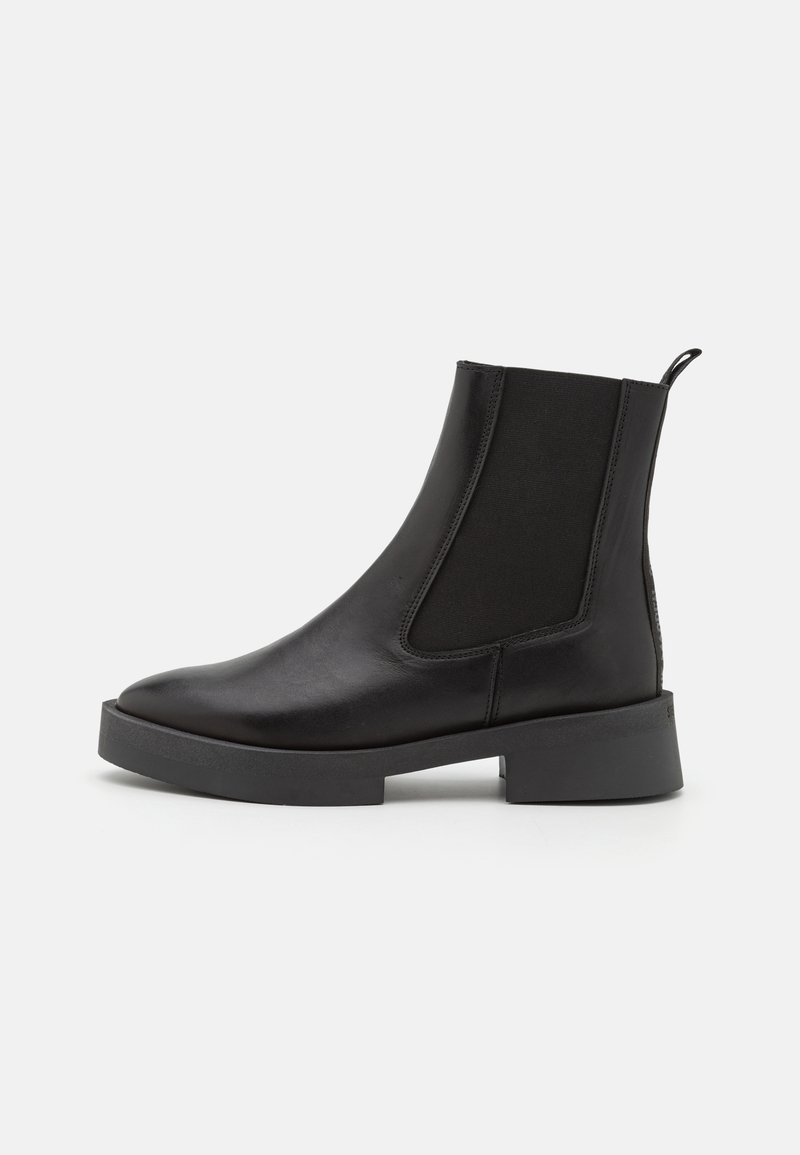 Botas de tobillo de cuero negro con paneles laterales elásticos, punta redondeada y suela de goma gruesa. Acabado suave con una lengüeta en la parte trasera.