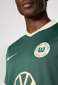 Roheline jalgpallipaita tekstuurses pinnas, V-kaelusega, kreemivärvi krae, Nike logo ja VfL Wolfsburgi embleem.
