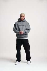 Gray hooded sweatshirt with black text reading "2Y STUDIOS," paired with loose black cargo pants and white sneakers, on a neutral background.