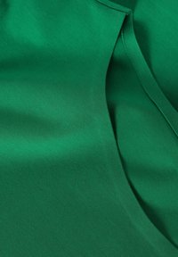 Tessuto verde, texture liscia, leggermente drappeggiato, con un bordo di colletto e un dettaglio delle cuciture, che presenta un colore uniforme senza motivi o accenti.