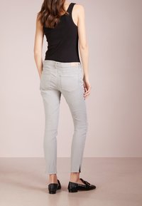 Ljusgrå, slim-fit jeans med bakfickor och en klyvning vid ankeln. Matchas med en svart linne och svarta loafers.