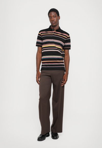 Polo noir à rayures avec des rayures horizontales multicolores, associé à un pantalon large marron et des chaussures noires. Texture en coton lisse.