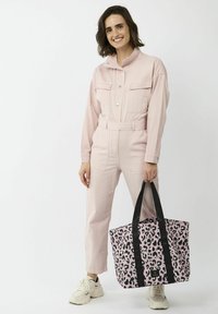 Roze denim jumpsuit met lange mouwen, voorzakken en een riem; zwarte en roze luipaardprint handtas met zwarte banden; witte sneakers.