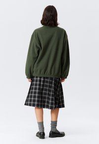 Grønn fleecejakke, rutete skjørt i svart og hvitt, teksturerte grå sokker og svarte sko. Uformelt antrekk med avslappet passform.