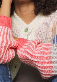 Pletený cardigan s kombinací měkkých bílých, růžových a světle modrých pruhů, s velkým iridescentním knoflíkem u výstřihu.