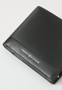 Portefeuille en cuir noir avec texture striée, dotée d'un bord cousu et d'un logo blanc. Design compact au look moderne.