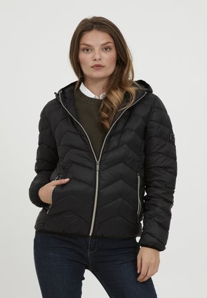 Zwarte pufferjack met een chevron-quiltpatroon, grijze ritsen, een capuchon en zijzakken; gedragen over een groene trui en een wit shirt.