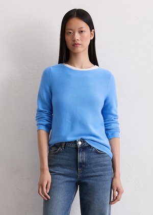 Jasnoniebieski sweter z długimi rękawami, okrągłym dekoltem i strukturalnym materiałem, w połączeniu z ciemnoniebieskimi dżinsami. Prosty i nowoczesny design.