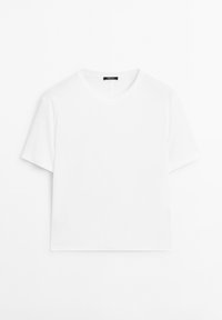Jednoduché bílé tričko s krátkým rukávem a kulatým výstřihem leží rovně s malou černou designerskou etiketou na zadní straně límce.